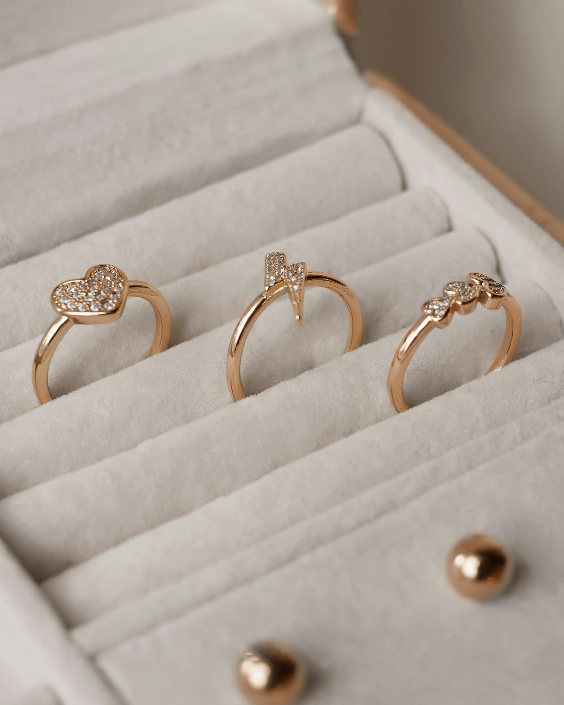 Three fine rose-gold rings set with small stones, resting in an ivory velvet ring tray.