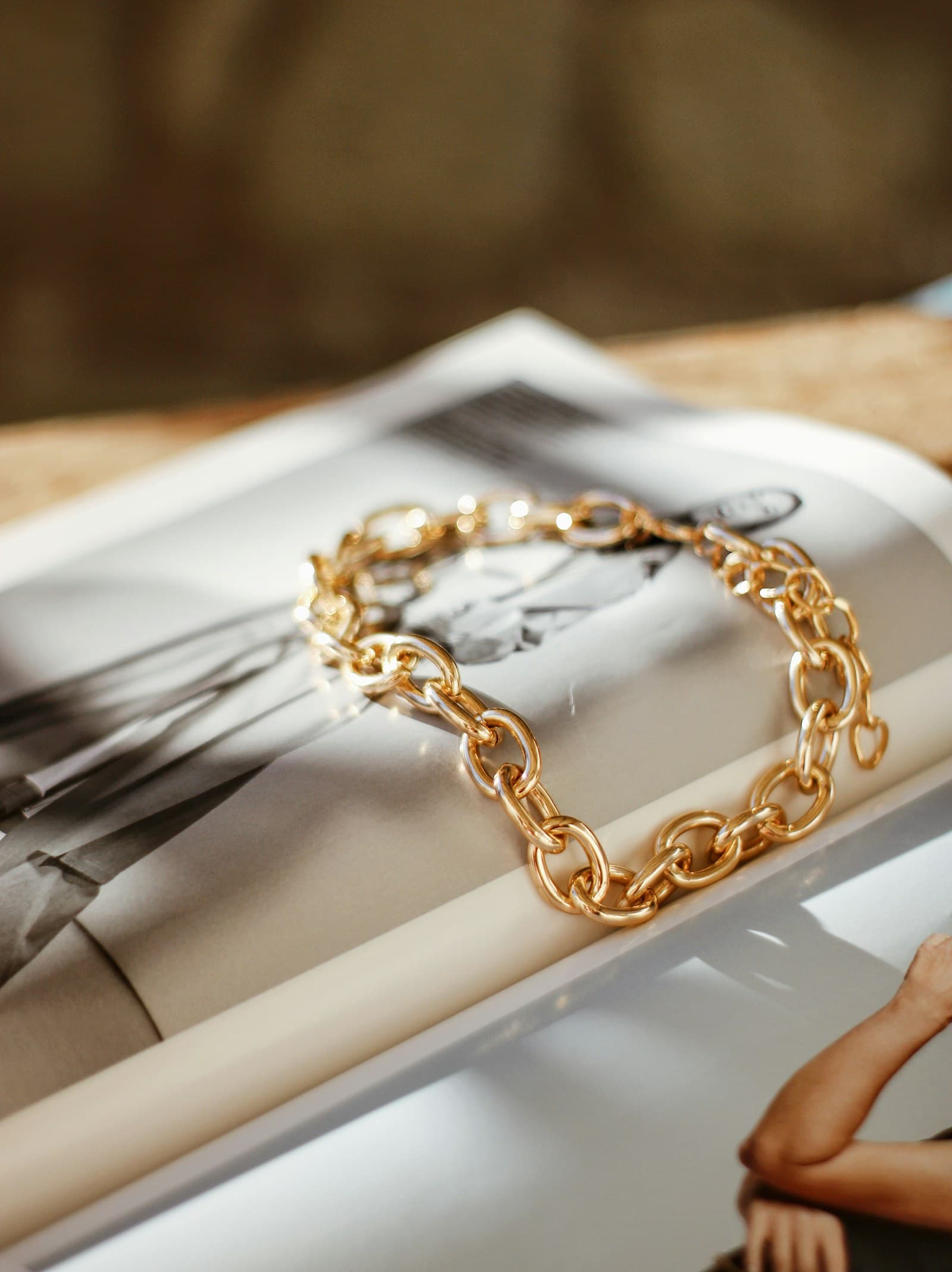 A gold chain bracelet resting on an open magazine.