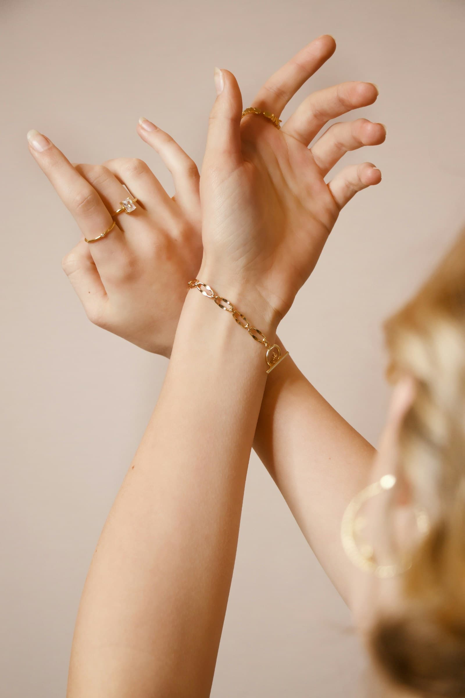 Two hands wearing fine gold bracelets.